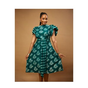 May include: A green dress with a white floral pattern and a matching belt. The dress has short sleeves with a ruffled design on one shoulder. The fabric has a tie-dye effect with vertical white stripes. The dress is knee-length.
