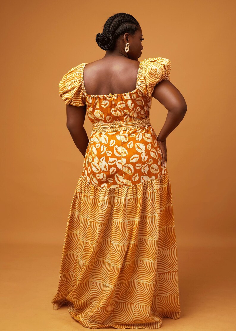 May include: A long, tiered maxi dress with a fitted bodice and puff sleeves. The dress is made of a yellow and white patterned fabric with a geometric design. The dress has a square neckline and a fitted waist.
