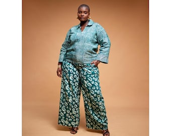 May include: A woman wearing a green and white patterned shirt and matching wide-leg pants. The pants have a white leaf print on a dark green background.
