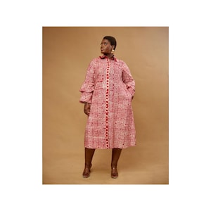 May include: A red and white patterned dress with a collared neckline, long sleeves, and a button-down front. The dress features a unique geometric design and is knee-length. The model is wearing brown heels.