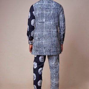 Pu&ograve; includere: Un set di camicia e pantaloni a maniche lunghe con motivo bianco e nero. La camicia presenta un motivo geometrico sul retro e un motivo ondulato sul davanti. I pantaloni hanno un motivo a cerchio grande su una gamba e un motivo ondulato sull'altra.
