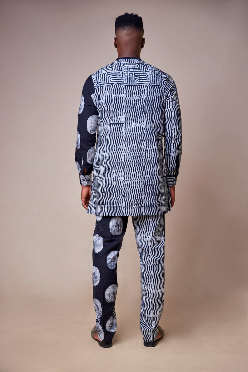 Pu&ograve; includere: Un set di camicia e pantaloni a maniche lunghe con motivo bianco e nero. La camicia presenta un motivo geometrico sul retro e un motivo ondulato sul davanti. I pantaloni hanno un motivo a cerchio grande su una gamba e un motivo ondulato sull'altra.