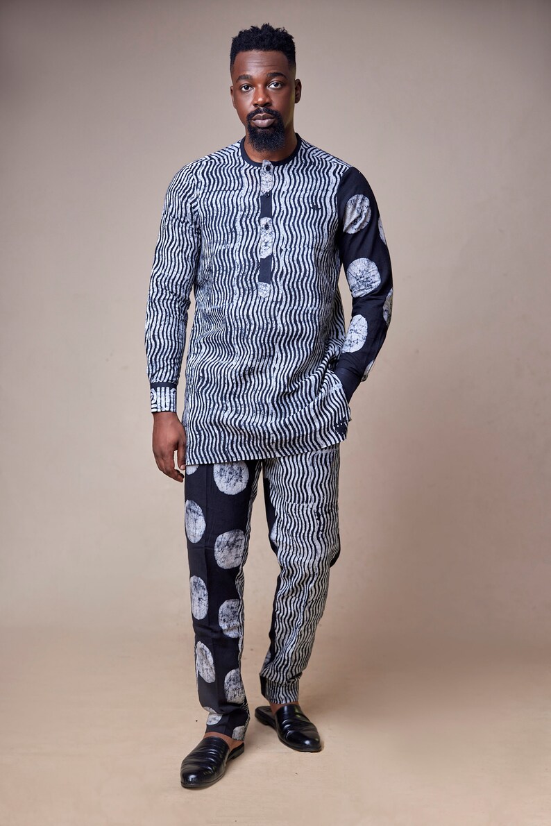 Pu&ograve; includere: Un uomo indossa una camicia a maniche lunghe e pantaloni abbinati con un motivo a righe bianche e nere. La camicia presenta un motivo a onde, mentre i pantaloni hanno un motivo a cerchi.