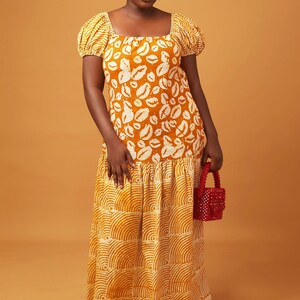 May include: A long yellow maxi dress with a white print of lips on the top half and a white print of curved lines on the bottom half. The dress has a square neckline and short puff sleeves.