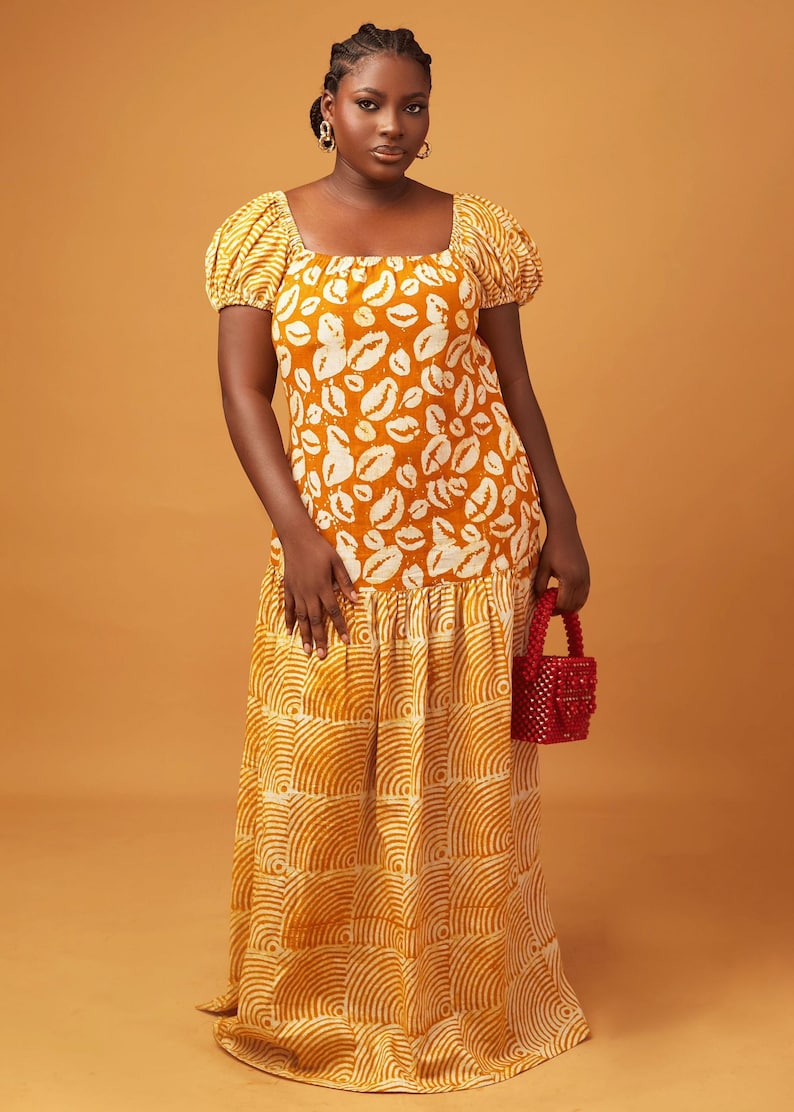 May include: A long yellow maxi dress with a white print of lips on the top half and a white print of curved lines on the bottom half. The dress has a square neckline and short puff sleeves.