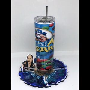 May include: A stainless steel tumbler with a blue and white design featuring a cartoon character and the text "Oops! All Berries". The tumbler is on a blue and green resin coaster.