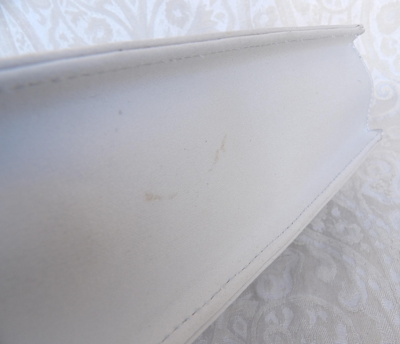 Puede incluir: Primer plano de un libro blanco con una cubierta texturizada. El lomo del libro es visible, mostrando la encuadernaci&oacute;n cosida. La cubierta tiene algunas peque&ntilde;as marcas. El libro est&aacute; sobre un fondo estampado.