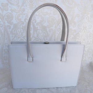 Puede incluir: Un bolso gris claro con dos asas superiores. El bolso rectangular tiene un cierre plateado y est&aacute; hecho de un material liso. Las asas est&aacute;n unidas a la parte superior de la bolsa con peque&ntilde;as fijaciones rectangulares.