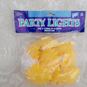 Op de afbeelding: Een pakket gele feestverlichting in een doorzichtige plastic zak. De verpakking heeft een blauwe en paarse kop met de woorden "PARTY LIGHTS" in teal. De koptekst vermeldt ook "EEN 4,27 m STRING VAN 10 LICHTEN BINNEN GEBRUIK".