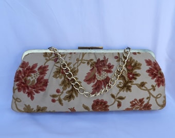 May include: A vintage-style clutch purse with a floral pattern in shades of red, brown, and green on a beige background. It features a gold-tone chain strap and a clasp closure.