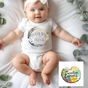 Puede incluir: Un body blanco para bebé con un diseño floral y el texto "Por este niño hemos orado 1 Sam 1:27".