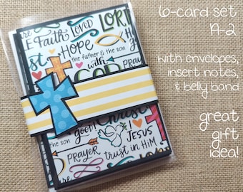 May include: A set of six A-2 greeting cards in a clear plastic sleeve, secured by a yellow and white striped belly band featuring a blue polka-dot cross cutout. The cards display religious text and illustrations including Faith, Hope, Love, and a dove.