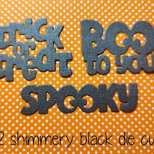 May include: Twelve shimmery black die cuts featuring the text trick or treat, boo to you, and spooky. The die cuts have a textured surface and are arranged on an orange background with a white polka dot pattern. The text is clearly legible.