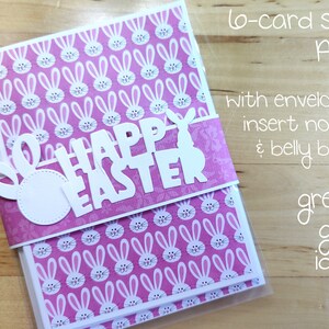 May include: A set of six blank greeting cards with pink bunny rabbit patterns and white envelopes. The cards are packaged in a clear plastic sleeve and feature a white die-cut bunny rabbit and the words "Happy Easter".