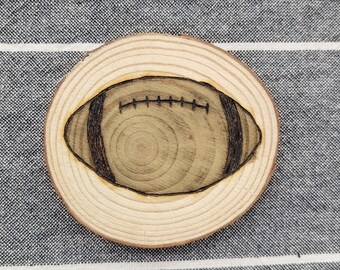 Könnte beinhalten: Ein runder Untersetzer aus Holz mit einem eingebrannten braunen und schwarzen Fußballdesign.