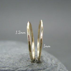 May include: Two gold hoop earrings, one 1 mm in diameter and the other 1.2 mm in diameter. Both earrings have a hammered texture.