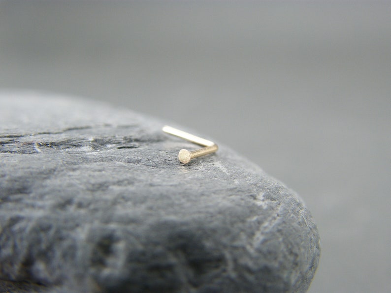 May include: A gold nose ring with a small, round bead at the end.