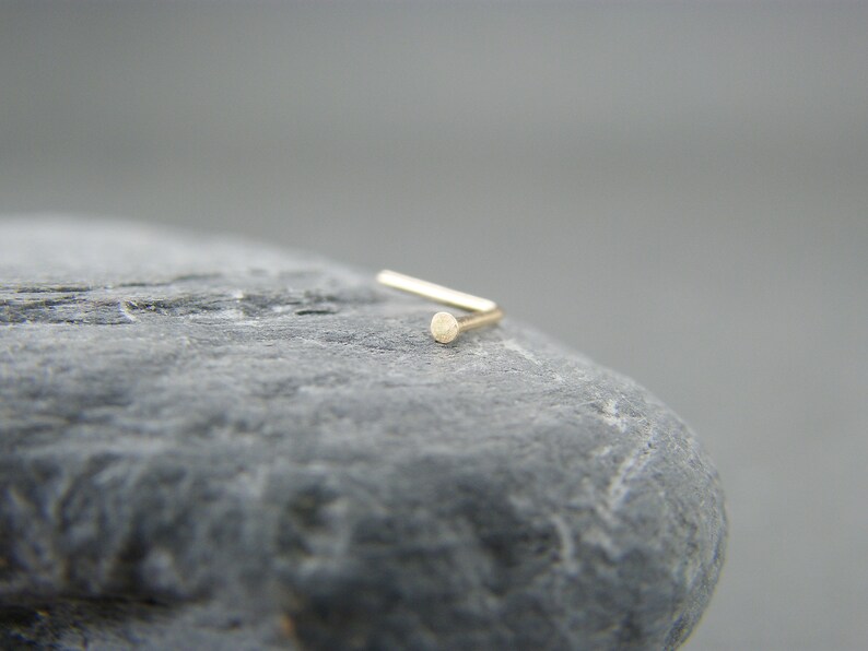 May include: A gold nose ring with a small, round bead at the end.