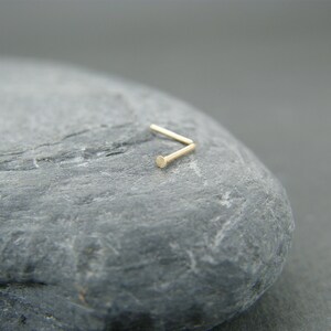May include: A gold nose ring with a small, round bead at the end.