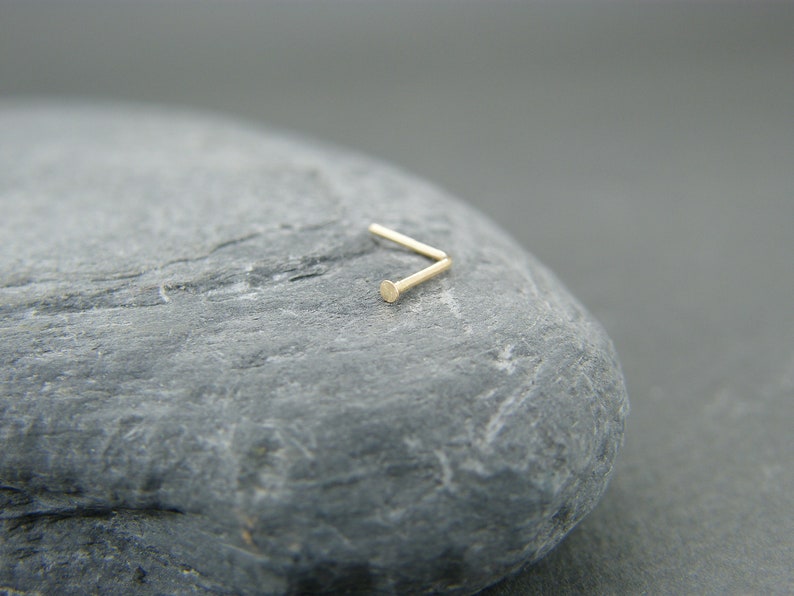 May include: A gold nose ring with a small, round bead at the end.