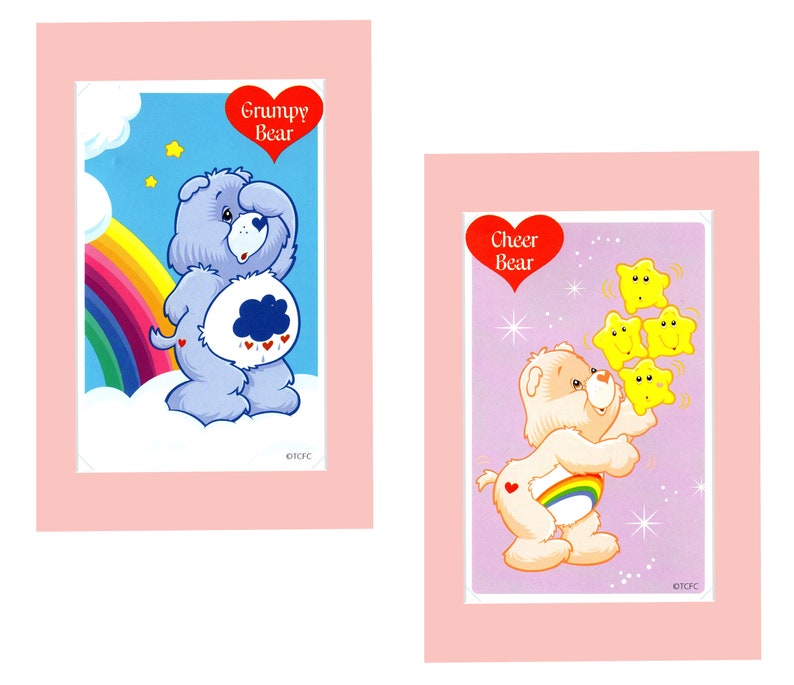 Pu&ograve; includere: Due carte con i personaggi di Care Bear. La carta a sinistra presenta Grumpy Bear, un orso blu con una nuvola di pioggia sul ventre. La carta a destra presenta Cheer Bear, un orso giallo con un arcobaleno sul ventre. Entrambe le carte hanno un cuore rosso con il nome dell'orso.
