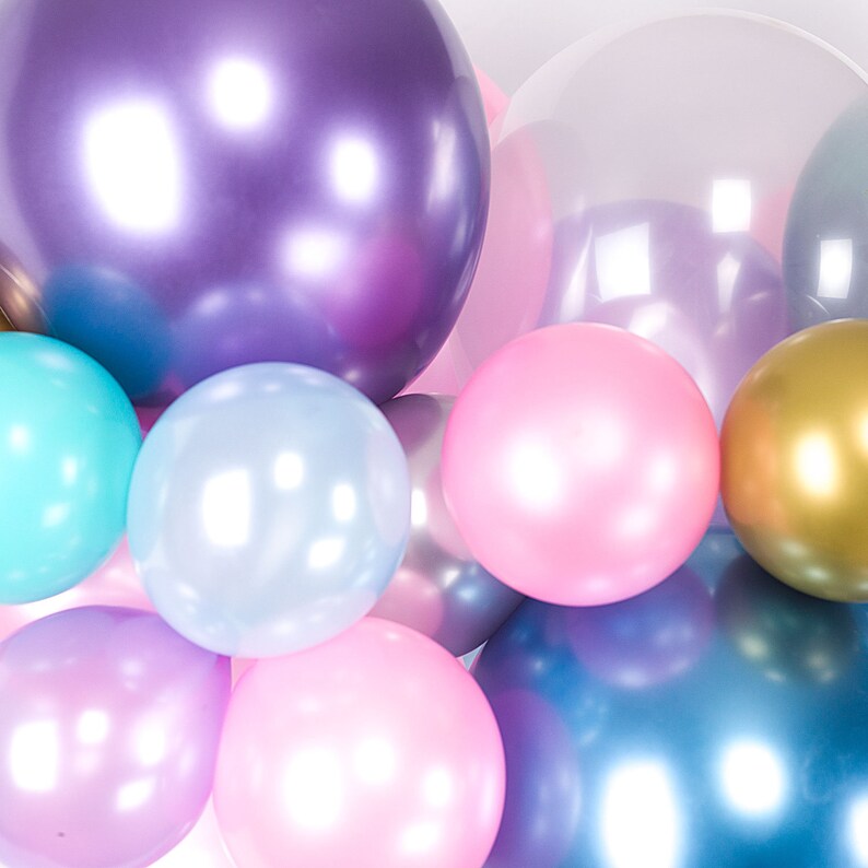Pu&ograve; includere: Un gruppo di palloncini iridescenti in vari colori pastello, tra cui viola, rosa, blu e oro. I palloncini sono disposti in cerchio, creando un'atmosfera festosa e gioiosa.