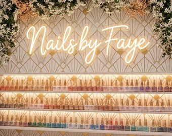 May include: A nail salon display featuring shelves of nail polish bottles in various colors. The wall is decorated with a geometric pattern and the neon sign "Nails by Faye". Floral arrangements adorn the top of the display.