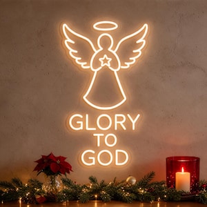 May include: A warm white neon sign featuring a stylised angel with wings, a halo, and a star, positioned above the text GLORY TO GOD in a clean sans-serif font. The light emits a soft glow against the wall, creating a bright focal point.