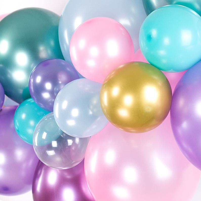 Pu&ograve; includere: Un gruppo di palloncini color pastello in tonalit&agrave; rosa, viola, blu e oro. I palloncini sono disposti in una forma sciolta e organica, creando un'atmosfera festosa e celebrativa.