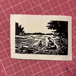 May include: A black and white linocut print depicting two figures in a lake or river. One figure is seated on a rock, while the other is in the water. Trees and water are also visible.