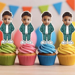 May include: Four cupcakes with colorful frosting and decorative toppers of a young child in a teal tracksuit. The cupcakes have green, pink, blue, and yellow frosting, with matching cupcake liners. Party decorations are in the background.