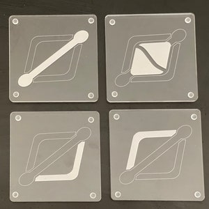 May include: A set of four square, clear acrylic coasters. Each coaster has a unique white geometric design. The designs include diagonal lines, curved shapes, and a central white shape. Small, clear, circular feet are at each corner.