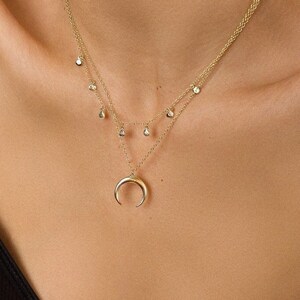 Puede incluir: Un collar de oro con un colgante de media luna y una cadena delicada con peque&ntilde;os detalles de diamantes.