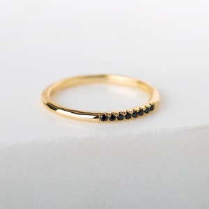 May include: A thin gold band ring with a row of small black gemstones.