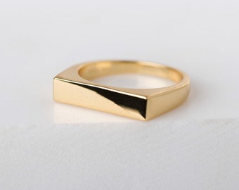 May include: A gold-colored ring with a rectangular band.