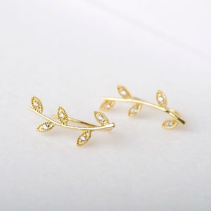 May include: A pair of gold leaf ear cuffs with small clear stones. The cuffs are shaped like a branch with leaves.