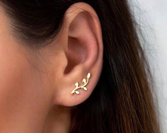 May include: Gold leaf ear climber earrings. The earrings are shaped like a branch with small leaves. The earrings are worn in the upper part of the ear.
