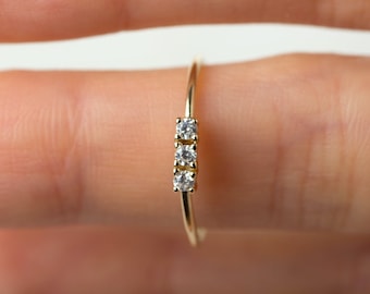 May include: A delicate gold ring with three small, clear diamonds set in a row.