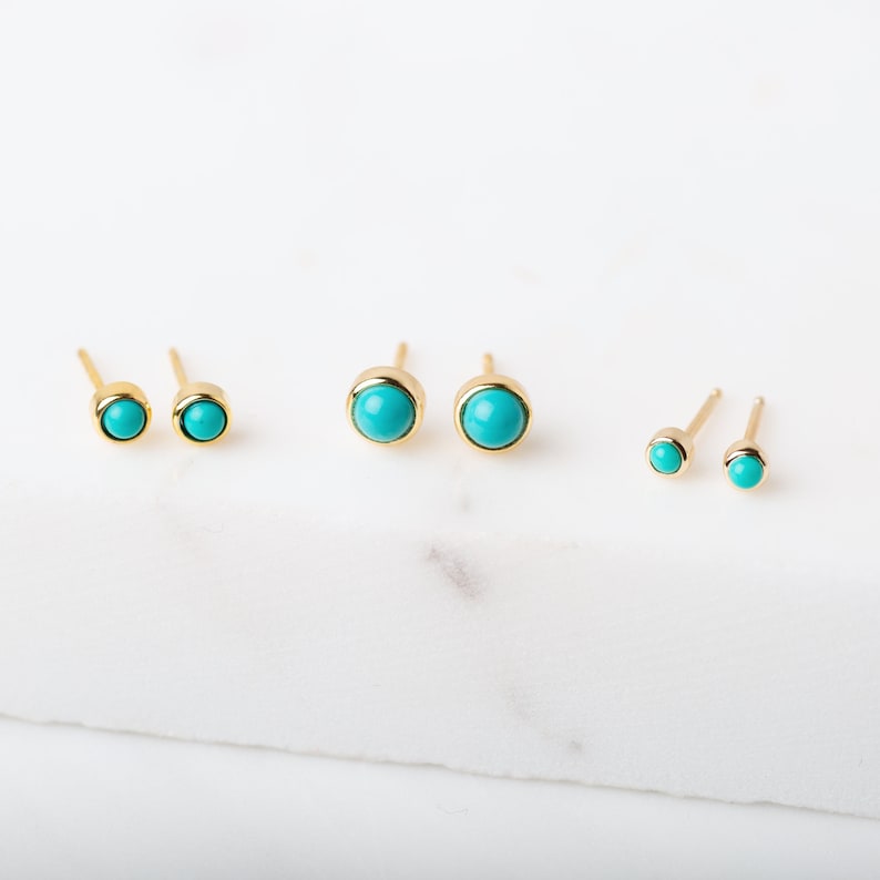 May include: Three pairs of gold stud earrings with turquoise stones. The earrings are different sizes.