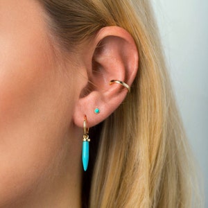 May include: A woman wearing a turquoise stone earring with a gold hoop and a small turquoise stone stud earring. The hoop earring has a pointed turquoise stone dangle. The text "2.5mm" is visible in the top right corner of the image.