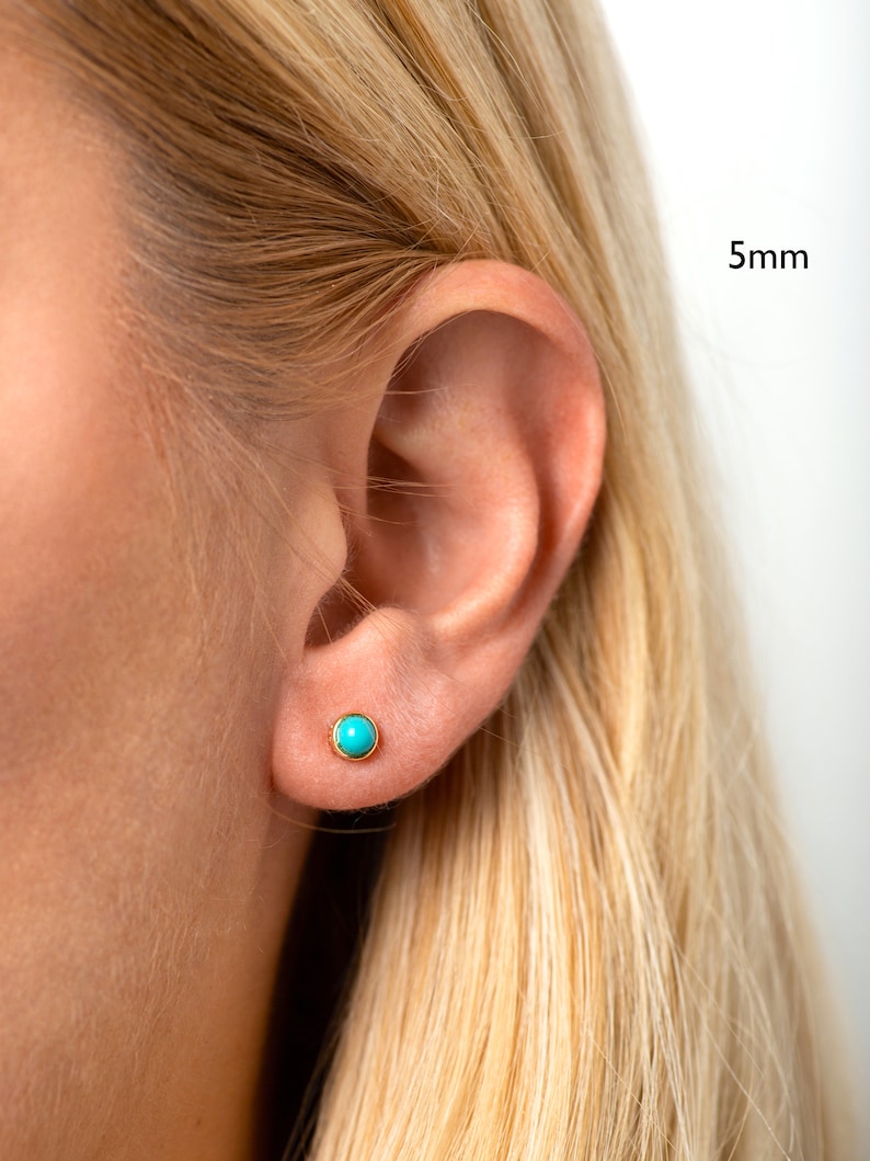 May include: A close-up of a person's ear with a small turquoise gemstone earring. The earring is 5mm in diameter.
