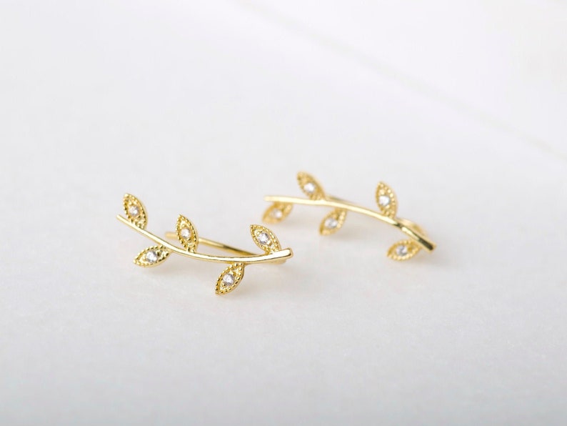 May include: A pair of gold leaf ear cuffs with small clear stones. The cuffs are shaped like a branch with leaves.