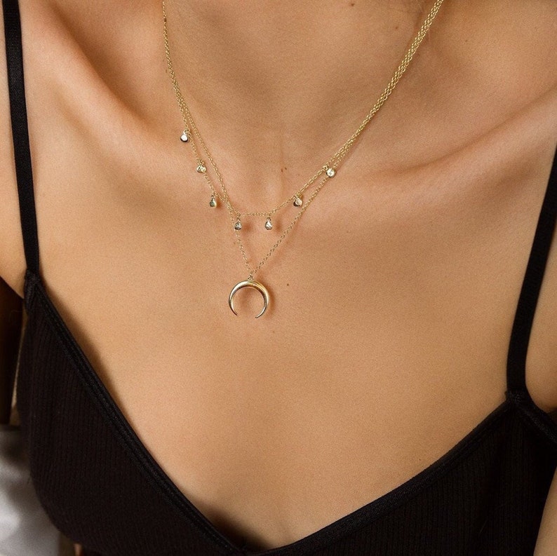 Puede incluir: Un collar de oro con un colgante de media luna y una cadena delicada con peque&ntilde;os detalles de diamantes.