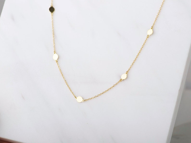 Puede incluir: Un collar de cadena de oro con peque&ntilde;os discos redondos como acentos.