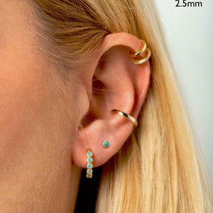 May include: Gold hoop earrings with turquoise stones. The earrings are 2.5 mm in diameter.