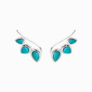May include: A pair of silver ear cuffs with turquoise stones. The cuffs are curved and have three stones each.