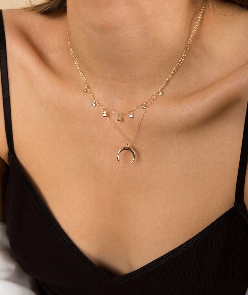 Puede incluir: Un collar de oro con un colgante de media luna y una cadena de varios niveles con peque&ntilde;os abalorios redondos.