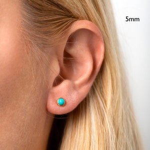 May include: Close-up of a person's ear with a small turquoise gemstone earring. The earring is set in gold and measures 5mm in diameter.