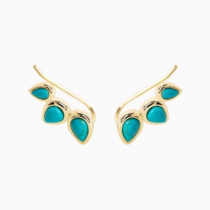 May include: A pair of gold ear climbers with turquoise teardrop-shaped stones. The climbers are designed to curve up the ear.