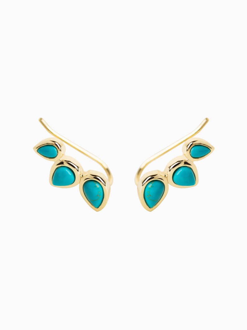 May include: A pair of gold ear climbers with turquoise teardrop-shaped stones. The climbers are designed to curve up the ear.